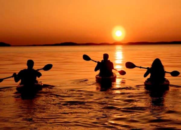 three people kayaking at sunset