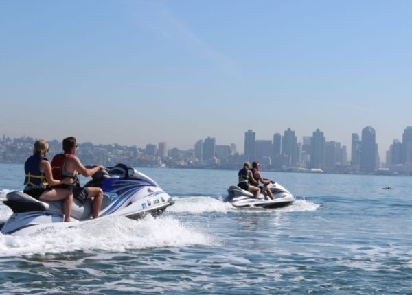 people riding two jet skis with city in background