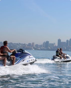 people ride two jet skis with city in background