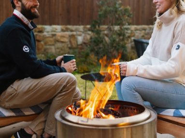 two people sit by a firepit wearing Safe Harbor sweaters