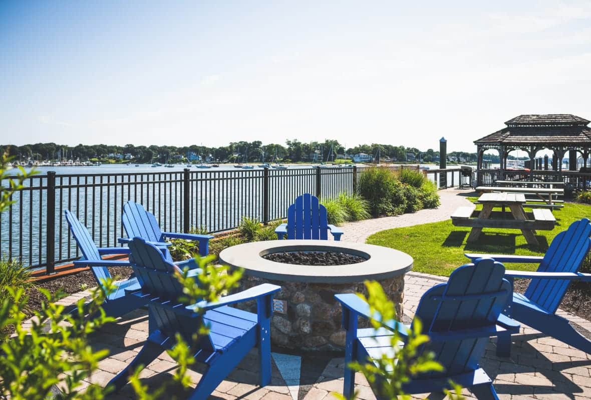 Stone fire pit surrounded by blue Adirondack chairs overlooking the water and a gazebo in the background