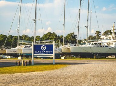 Safe Harbor Jarrett Bay sign with sailboats docked on land behind it
