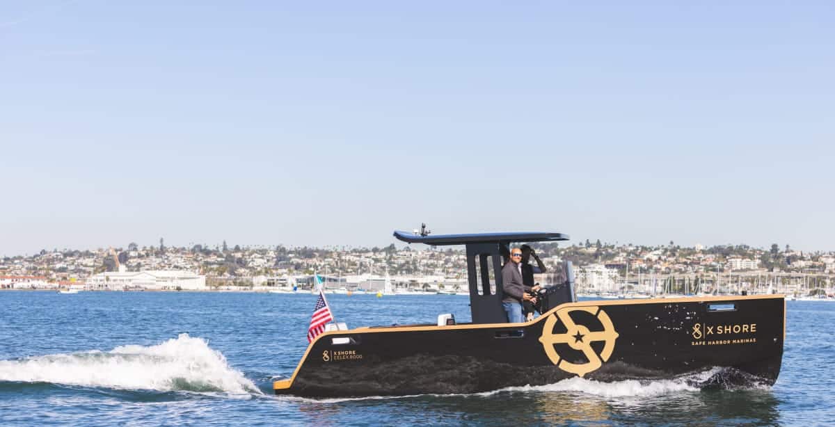x shore boat driving across the water with American flag on the back and SHM logo on the side