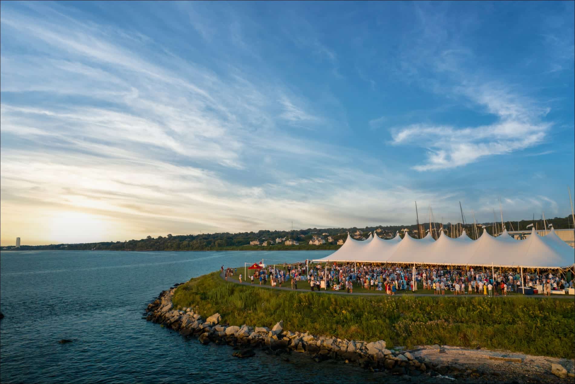 large crowd under a tent by the water at sunset